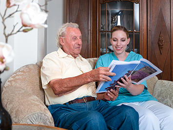 Altenpflegerin und Senior lesen in einer Zeitschrift