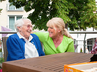 Betreuerin und Seniorin sitzen auf einer Bank